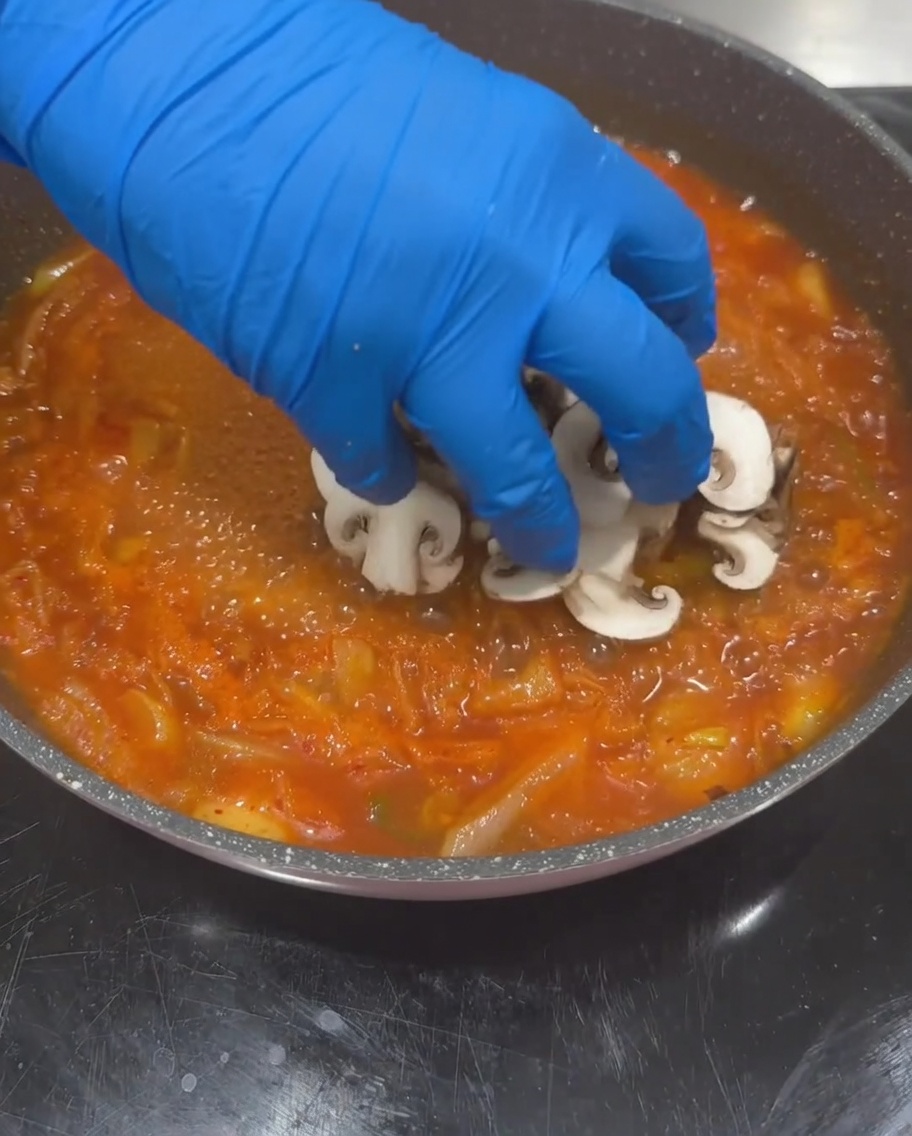 Sliced shiitake mushrooms, zucchini, and tofu being added to the boiling kimchi soup base.