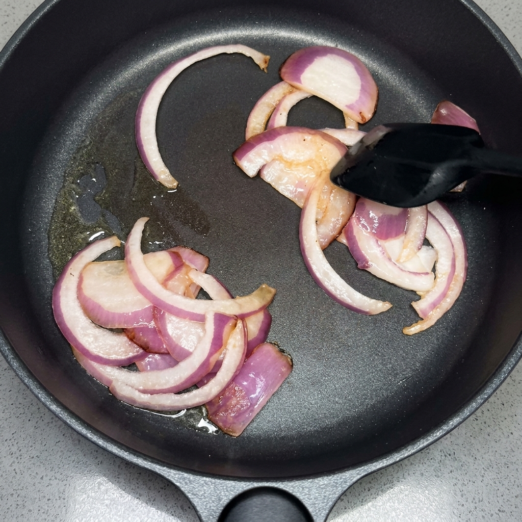 Slices of red onion being sautéed in a pan with a spatula.