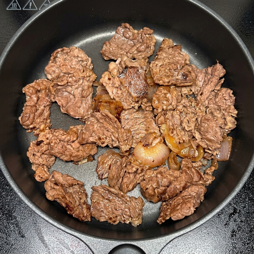 Kimchi pieces being stirred into the pan with beef and onions.
