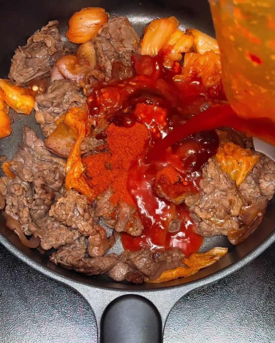 Water being poured into the pan containing the seasoned beef and kimchi mixture.