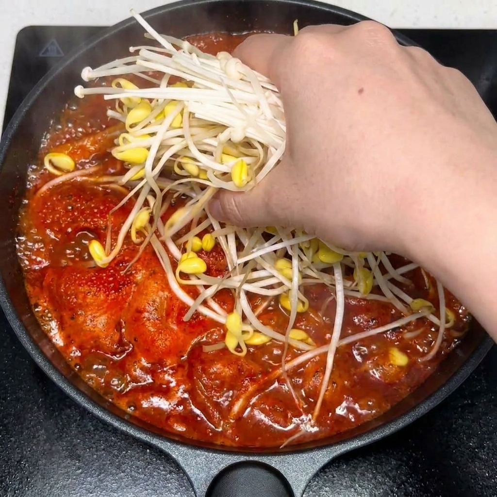 Minced garlic and seasonings being stirred into the red, spicy kimchi beef soup.