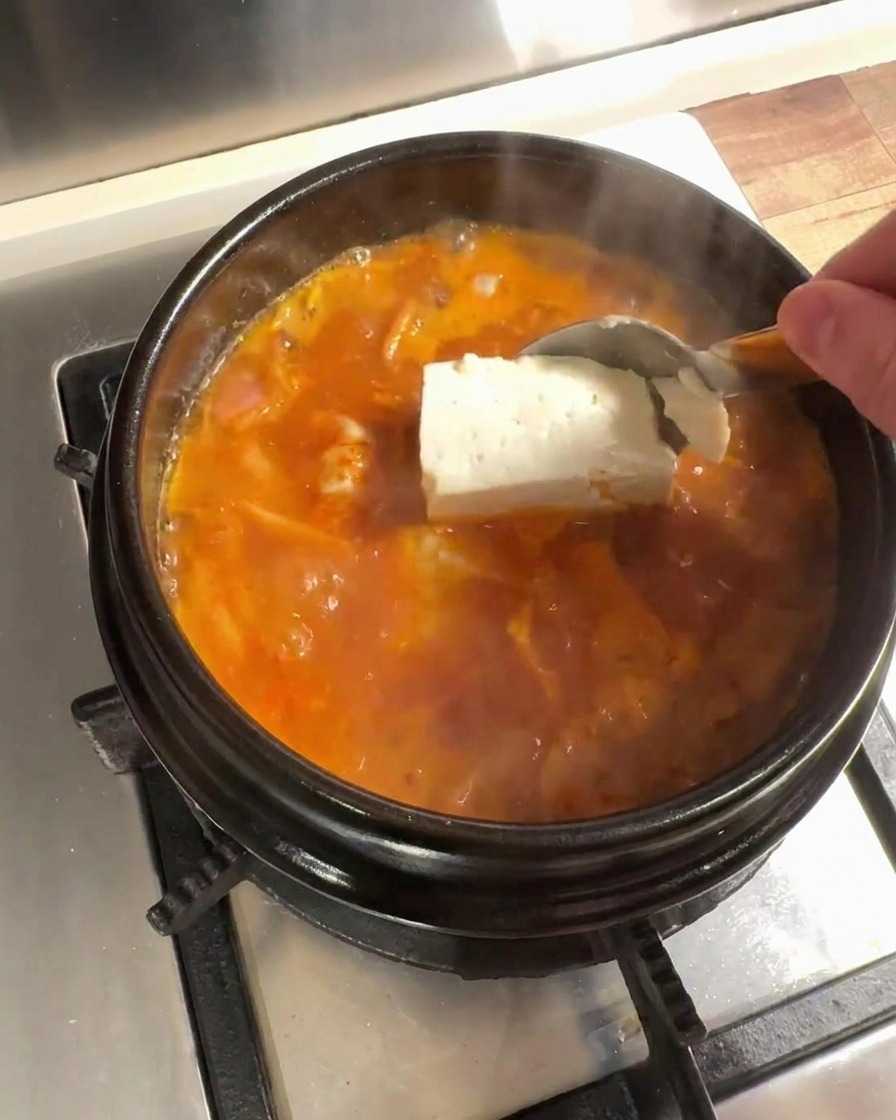 Large pieces of fresh tofu being added to the simmering kimchi broth.