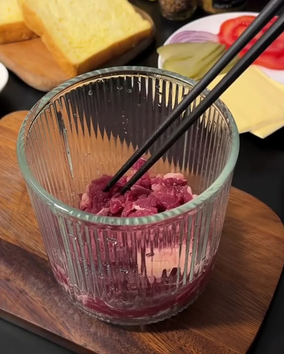 Fresh raw ground beef inside a glass manual food chopper, ready to be processed.