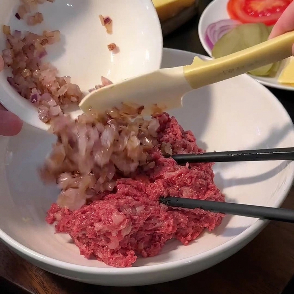 A bowl containing ground beef, breadcrumbs, salt, pepper, and sautéed onions before mixing.