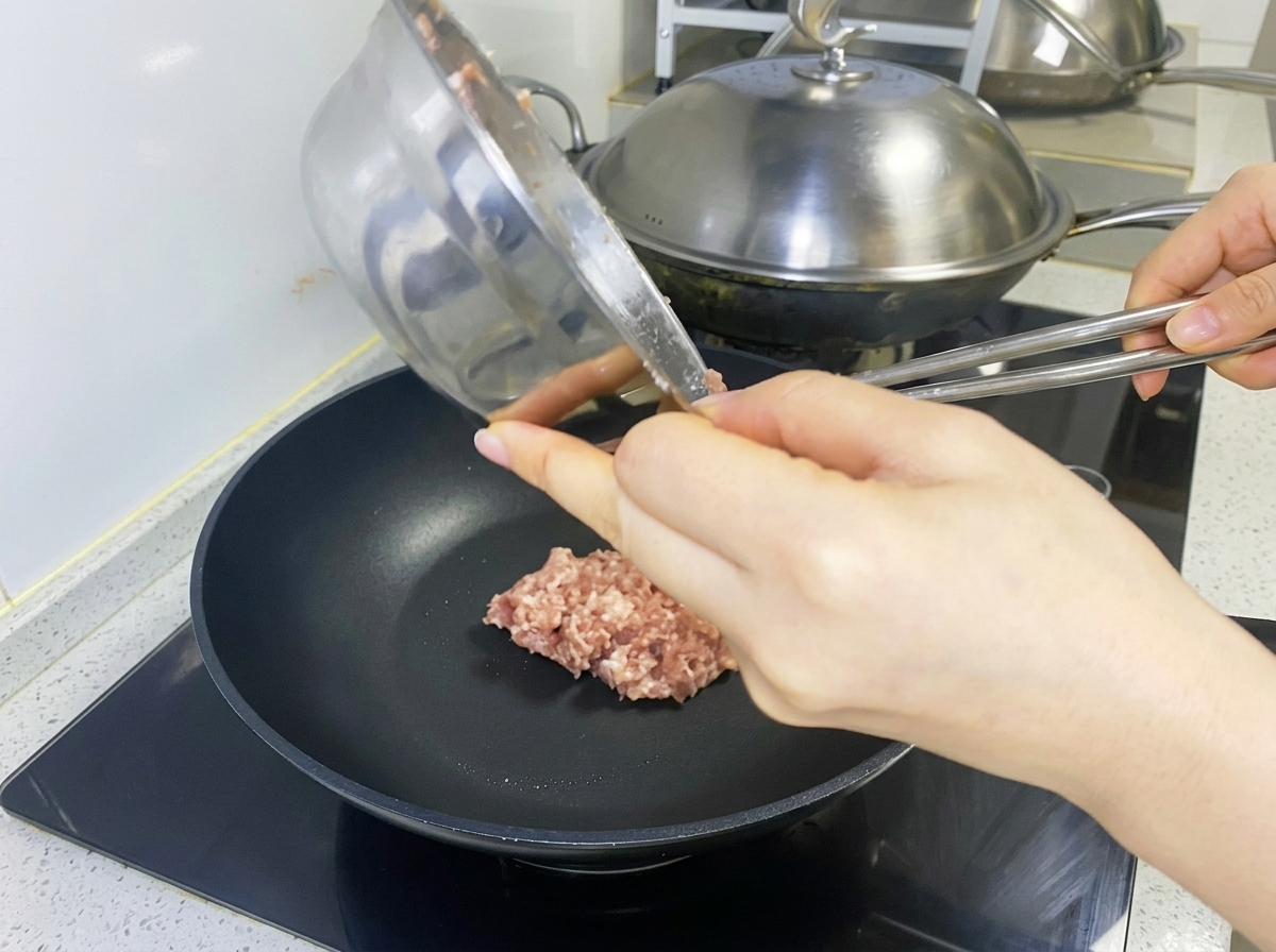 Seasoned raw meat mixture being placed into a black pan to form a patty.