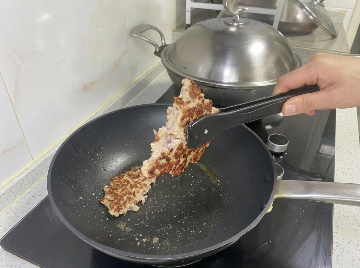A cooked, golden-brown pork patty being lifted from the pan with tongs.