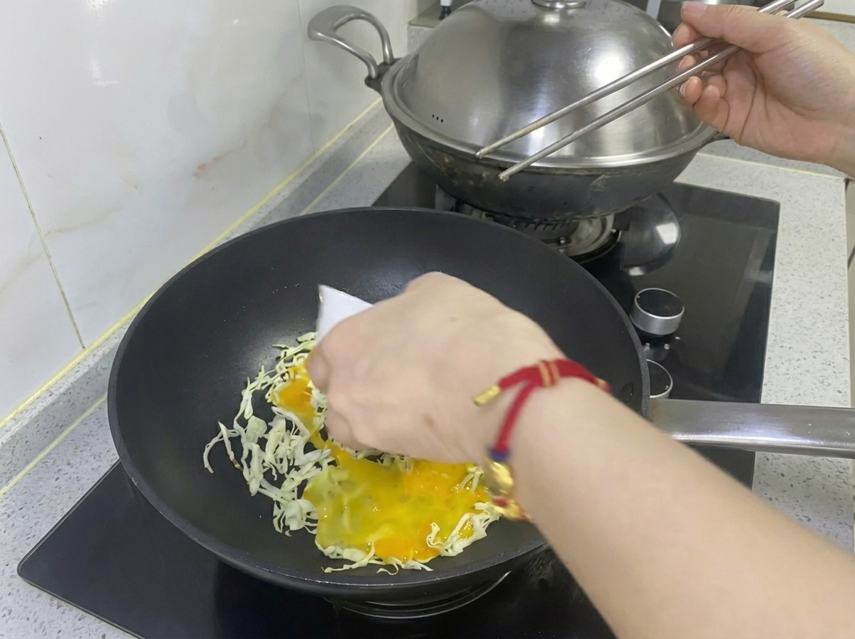 Beaten egg being poured over shredded cabbage in a frying pan.
