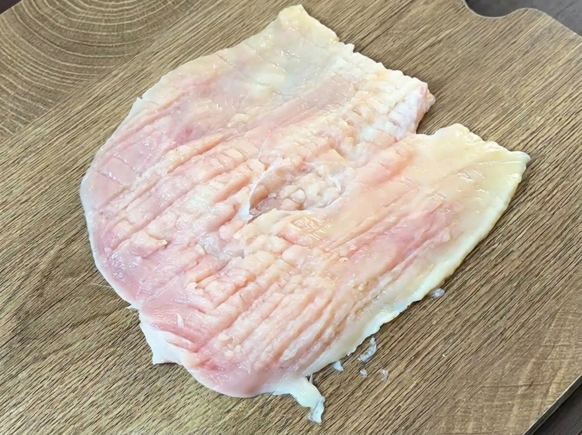 The back of a heavy knife being used to pound and flatten a raw butterflied chicken breast.