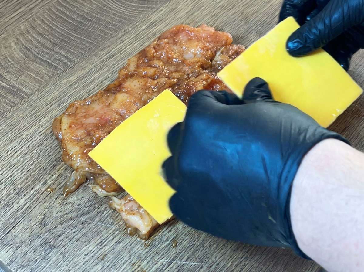 Yellow cheese slices placed on the center of the raw, marinated chicken breast.
