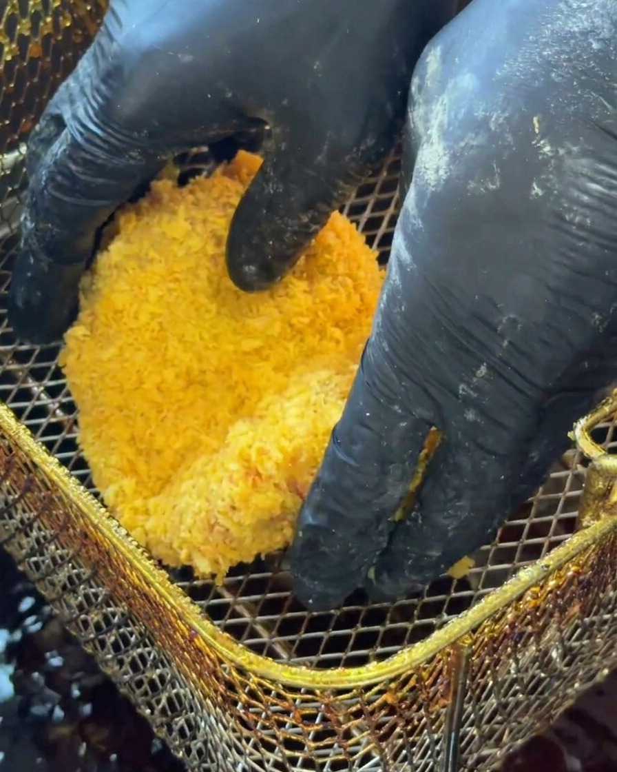 Breaded chicken patty being lowered into hot frying oil.