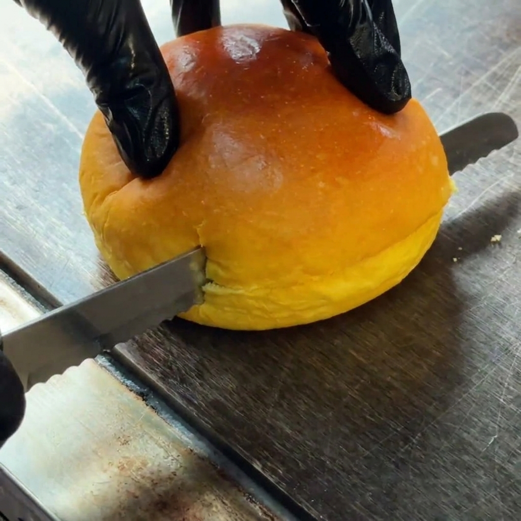 A burger bun being sliced horizontally in half.