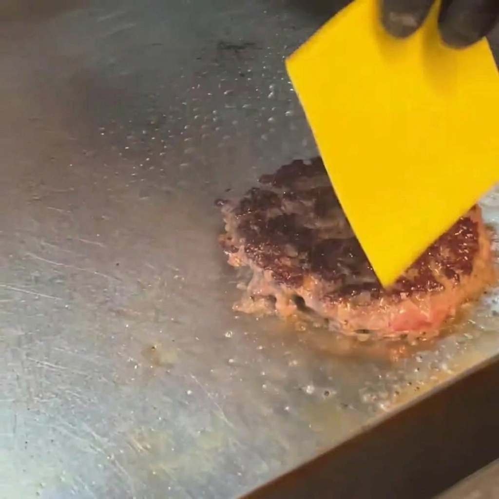 A slice of yellow cheese melting on top of a seared burger patty using a handheld culinary torch.