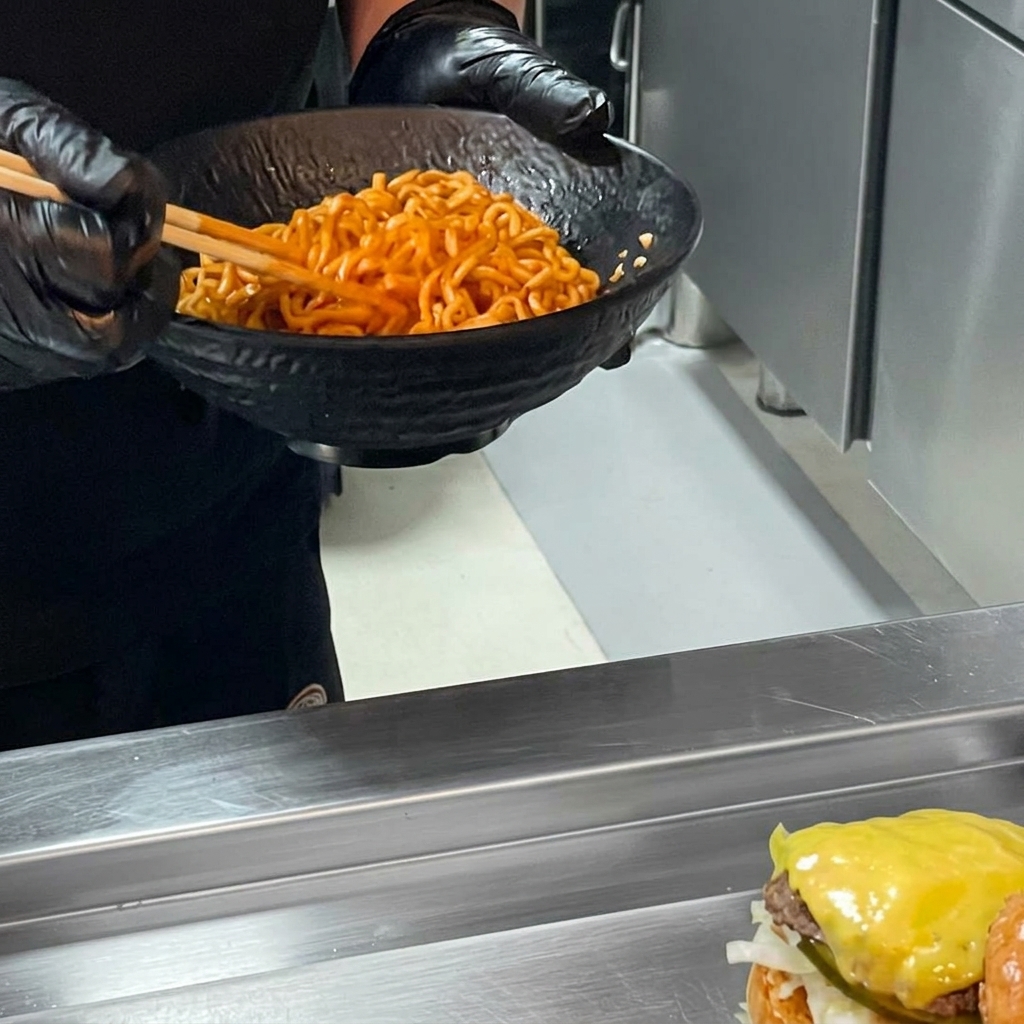 A spicy chicken ramen burger being finished by adding a large mound of spicy ramen noodles onto the beef patty and covering it with the top bun.