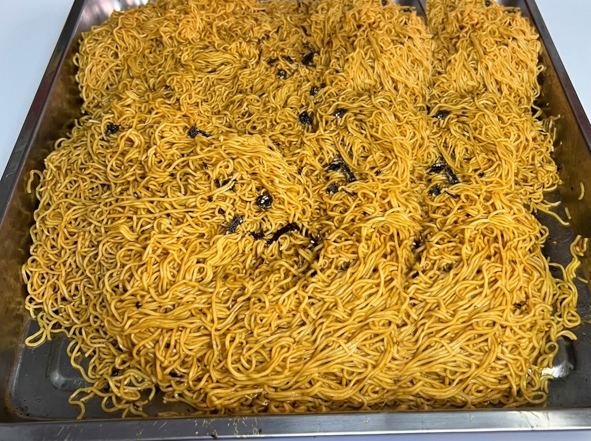 A large batch of cooked noodles spread out in a stainless steel tray.
