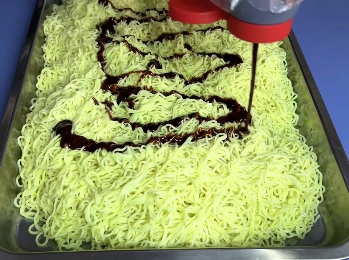 Non-spicy fire noodle sauce being squeezed from a bottle onto a bed of noodles.