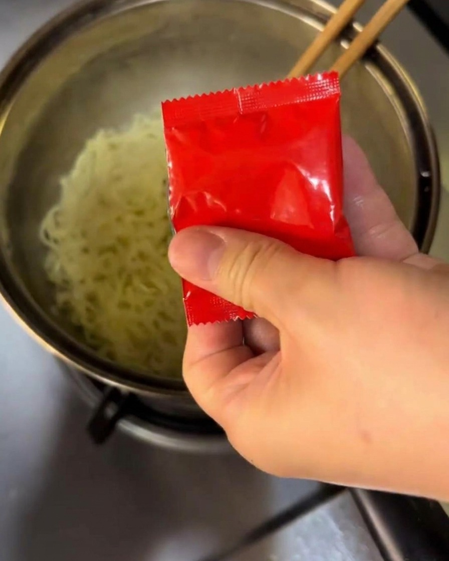Mixing seasoning and spicy sauce into boiling noodles in a pot.
