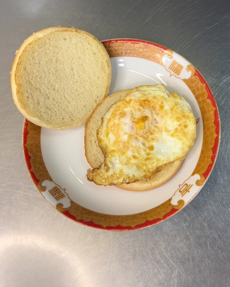A slice of yellow cheese placed on top of the fried egg inside the burger bun.