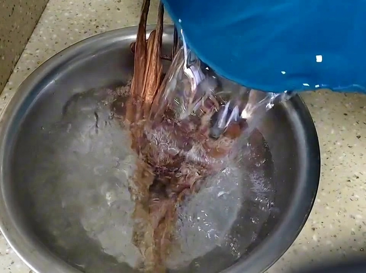 Water being poured over dried octopus and shiitake mushrooms to soak them in a metal bowl.