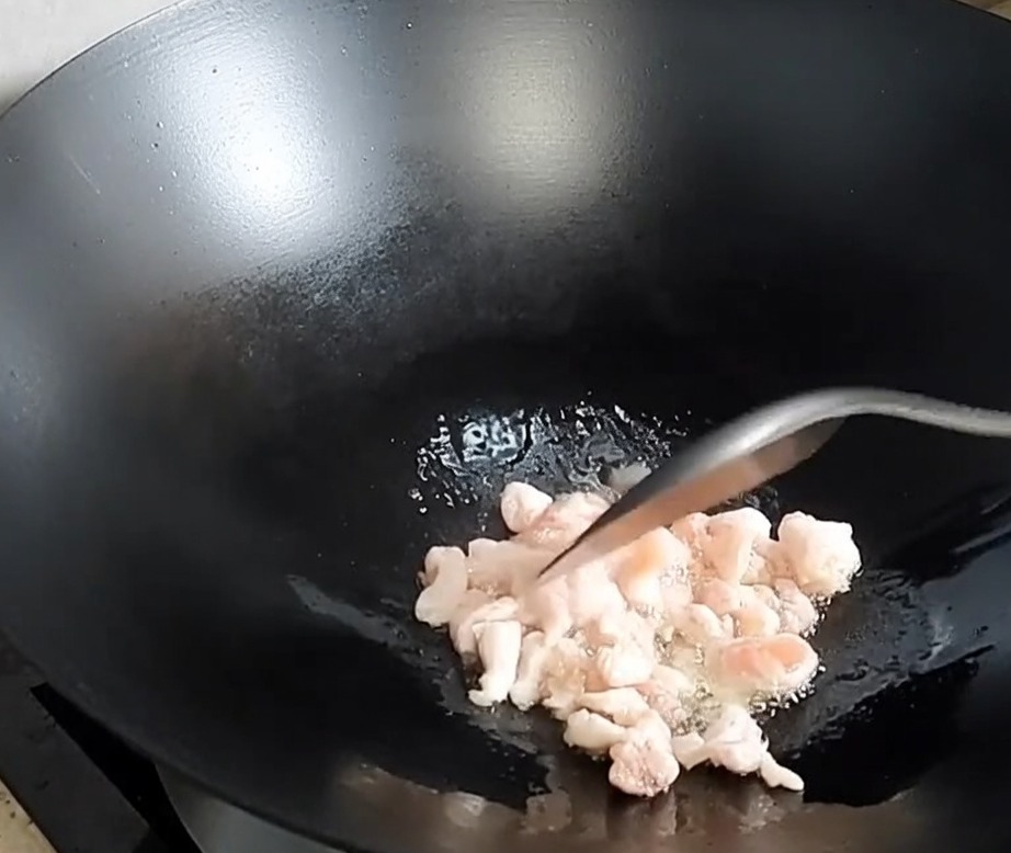 Diced pork belly browning and releasing fat in a hot wok.