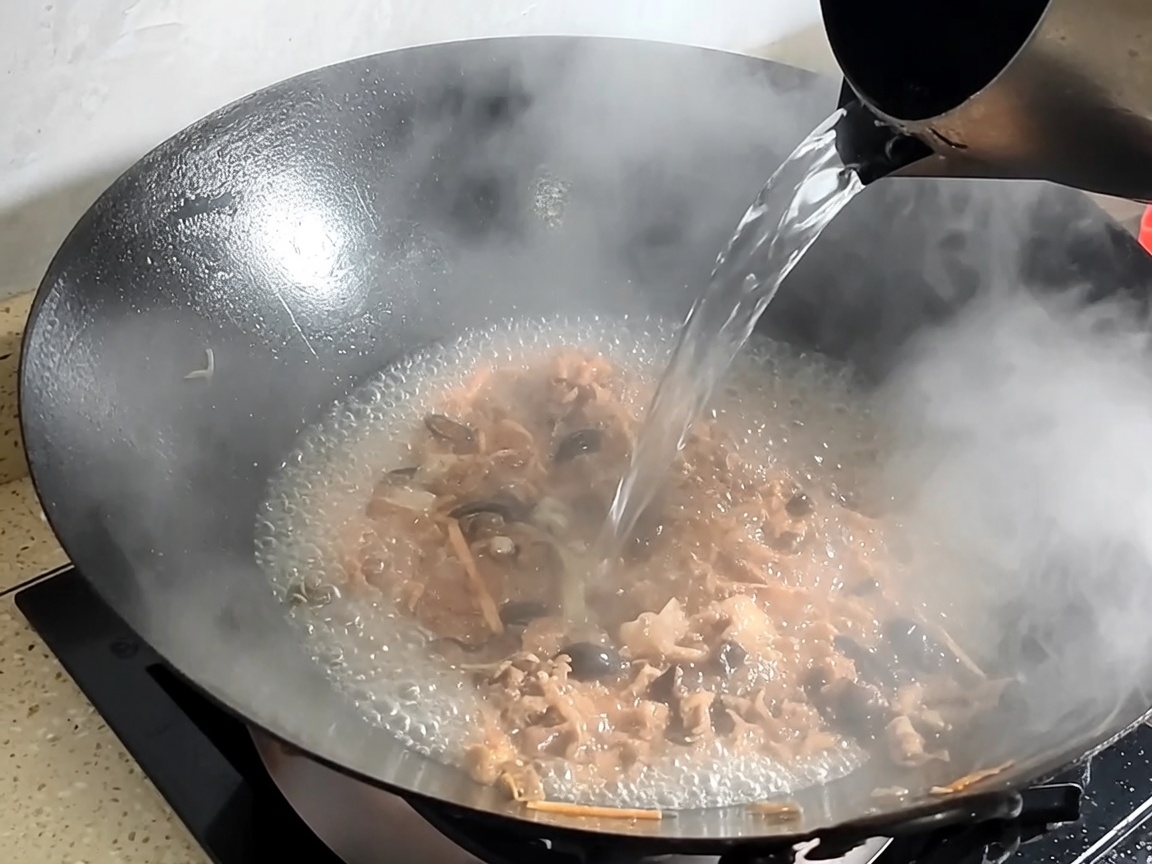 Water being poured into the wok with sautéed pork and mushrooms to form the broth.