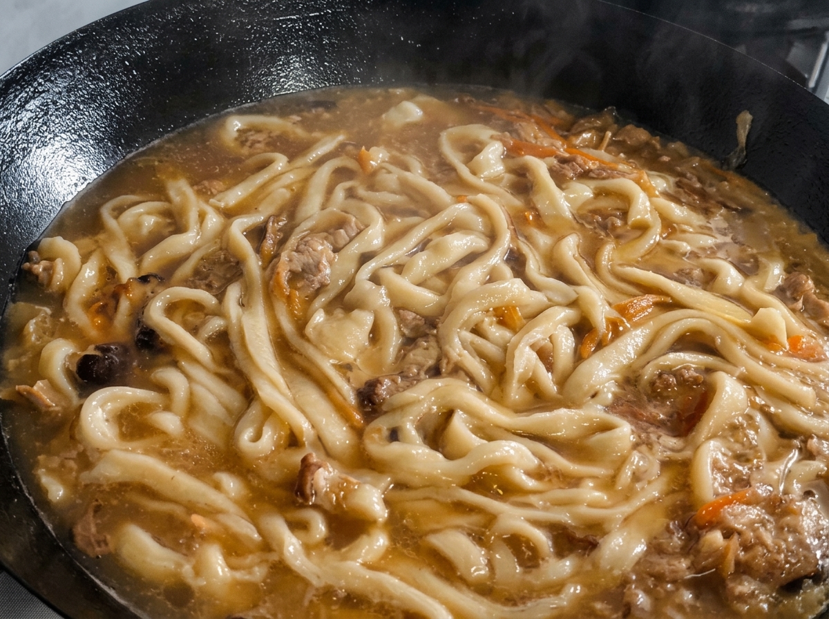 Chopped perilla leaves being scattered over the noodles and soup simmering in a wok.