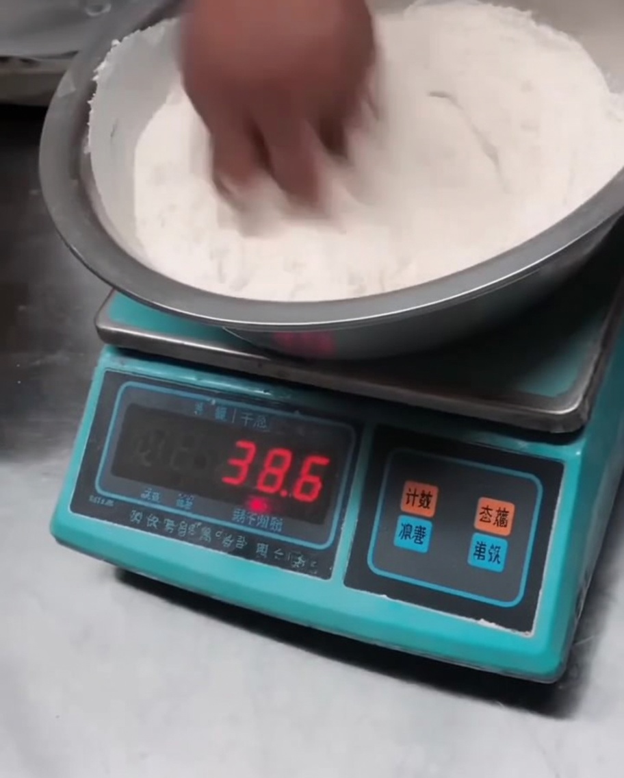 Dry flour being mixed with salt and alkaline powder in a large metal bowl.