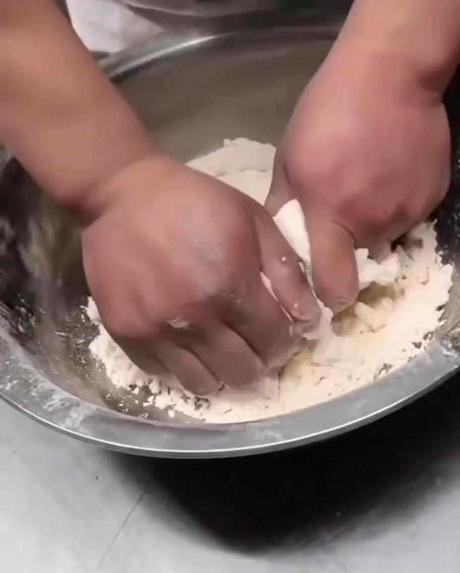 Hands pressing shaggy dough flakes together into a cohesive dough ball.