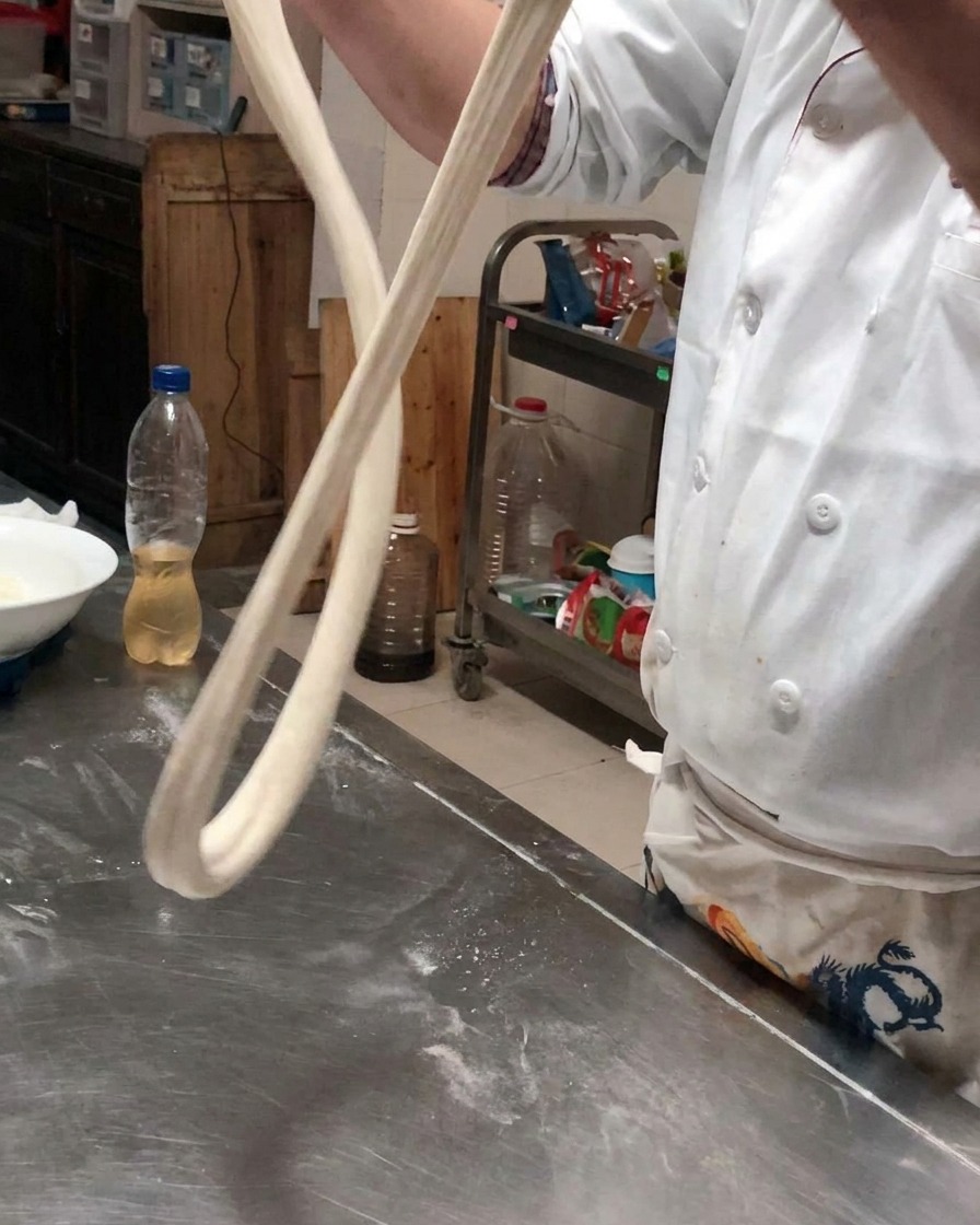 A long rope of dough held in the air to allow it to stretch under its own weight.