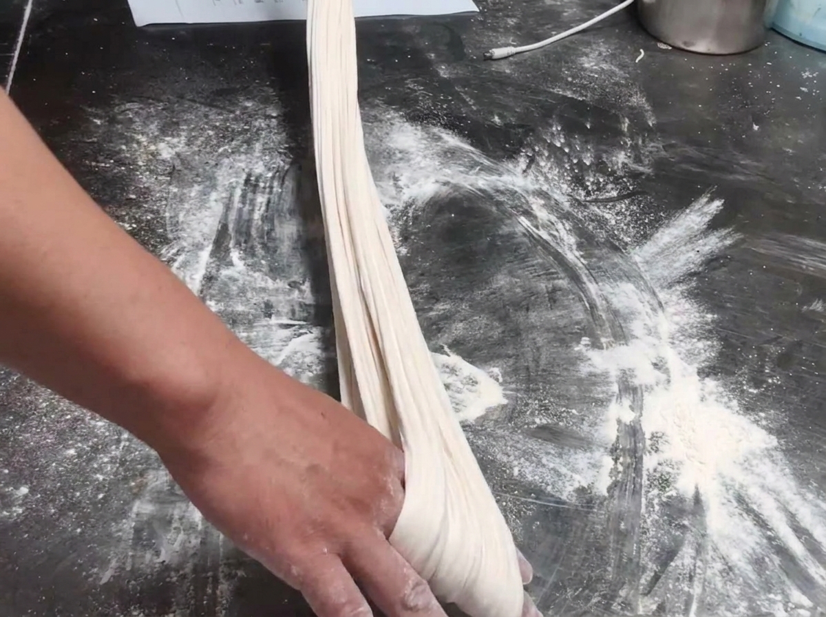 Dough rope being stretched and checked for thickness on a floured table.