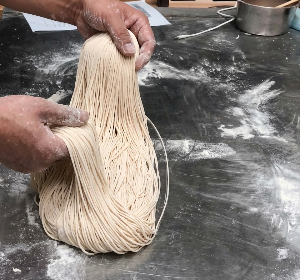 Freshly pulled long, thin noodle strands held up in the air.