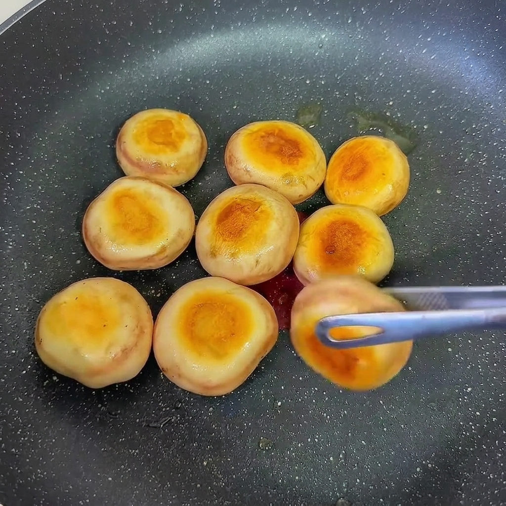 Mushroom caps stuffed with shrimp paste frying in a pan being flipped to brown the other side