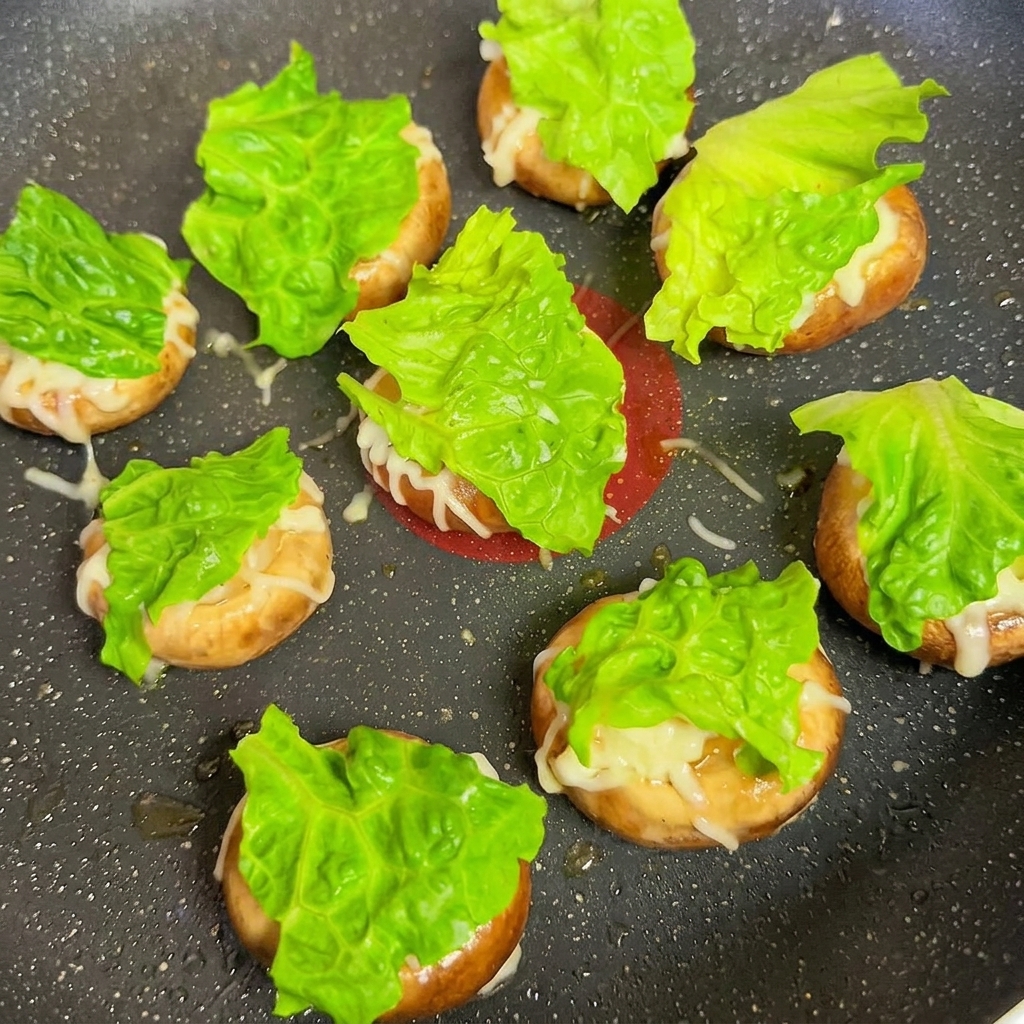 Mushroom caps topped with lettuce and cheese squares in a frying pan.