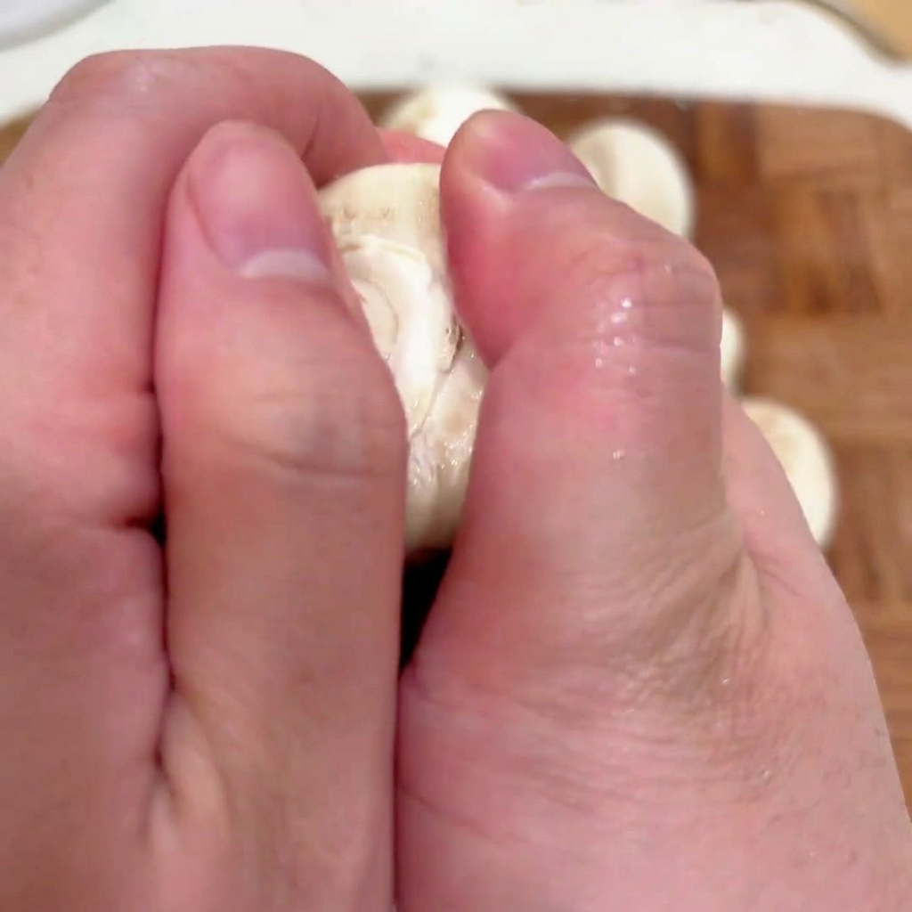 A close-up view of hands removing the stem from a fresh white mushroom cap to prepare it for stuffing.