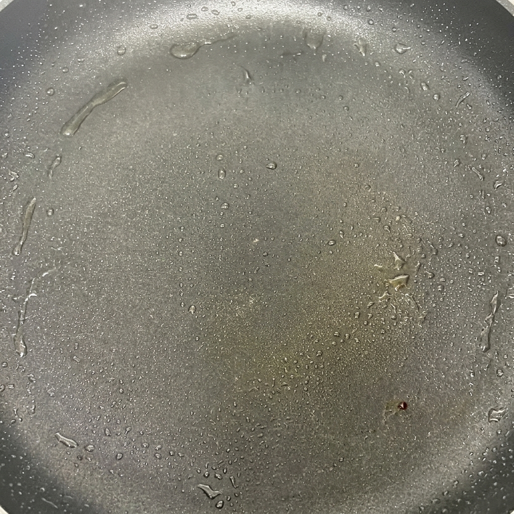Mushroom caps sizzling in a hot frying pan with oil, beginning to brown slightly.