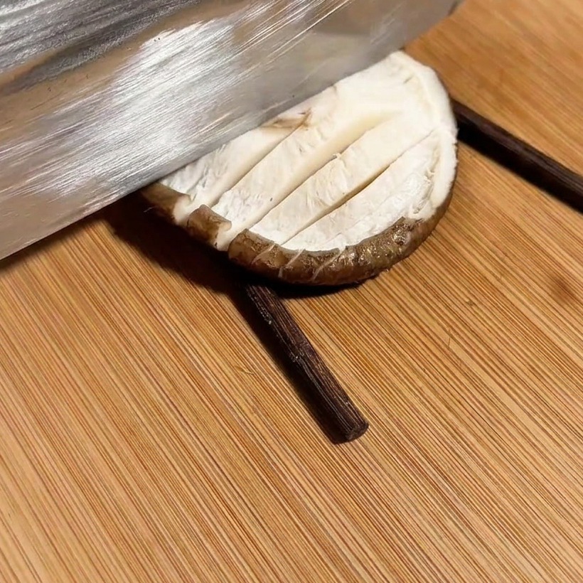 A knife cutting a cross-hatch pattern into a mushroom placed between two chopsticks.