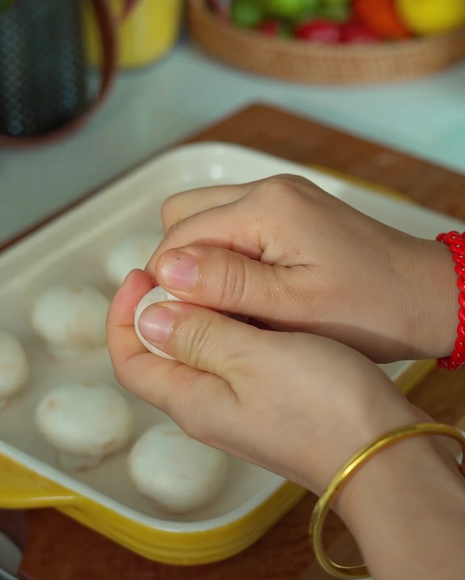 Hands carefully snapping the stem off a white button mushroom to create a hollow center.