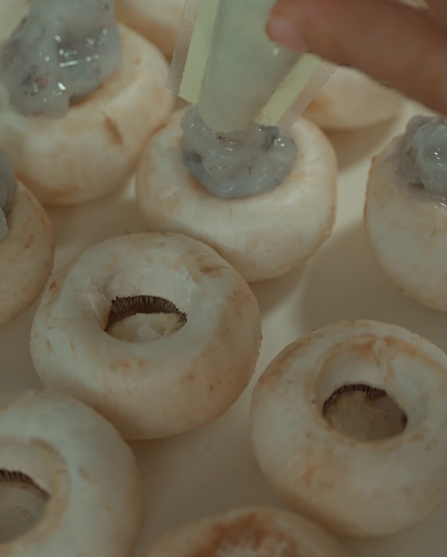 Shrimp paste being piped from a plastic bag into the hollow centers of cooked mushroom caps.