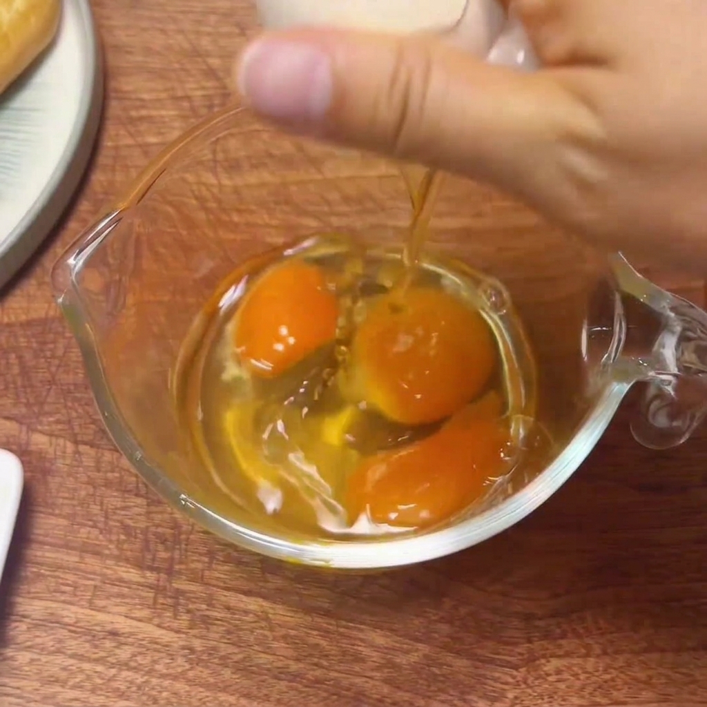 Fresh eggs being cracked into a glass measuring cup, ready to be beaten.