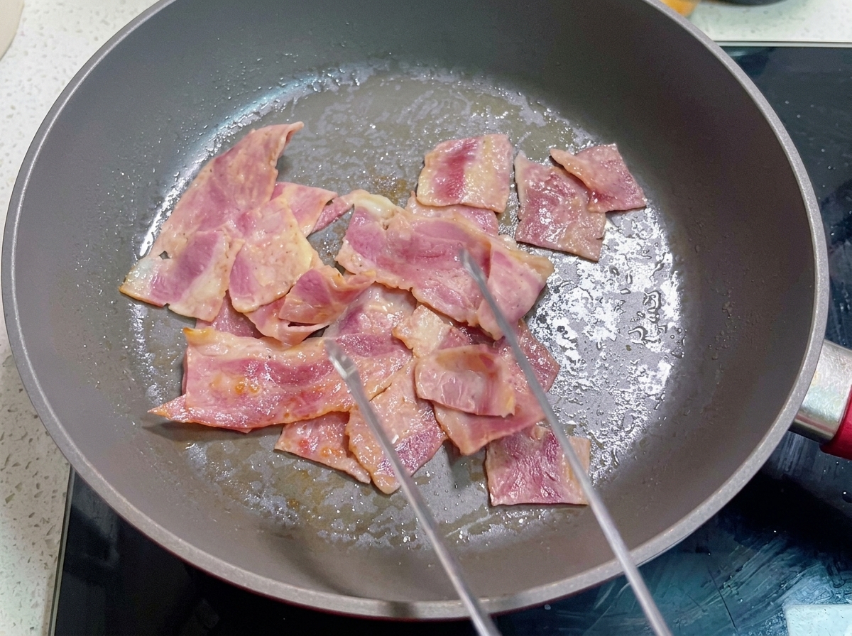 A pan containing cooked bacon with a beaten egg mixture being poured over it.