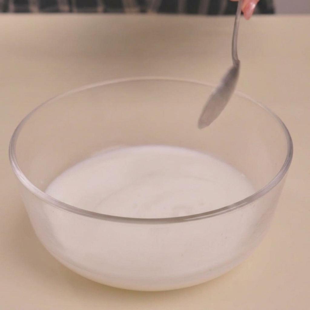 Milk being curdled in a glass bowl after adding vinegar, creating a buttermilk-like texture.