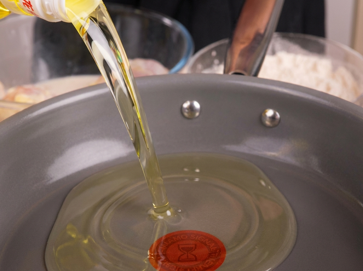 Cooking oil being poured into a frying pan, getting ready to be heated.