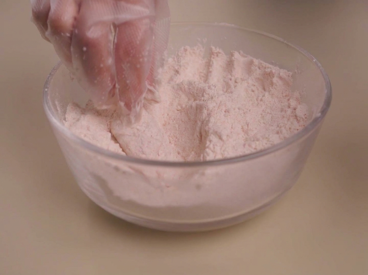 A piece of raw marinated chicken being coated in a bowl of dry seasoned flour.