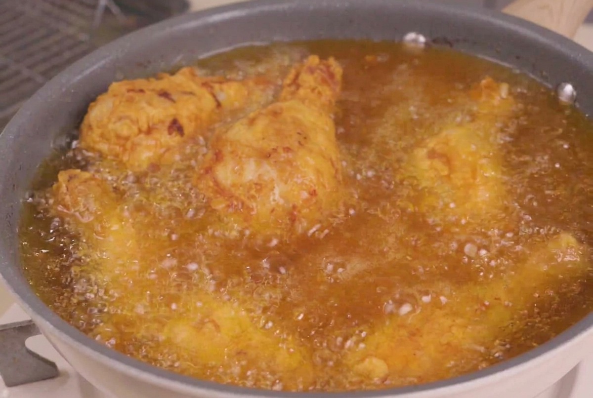 Fried chicken pieces being submerged into a pan of hot, bubbling oil for the final frying stage.