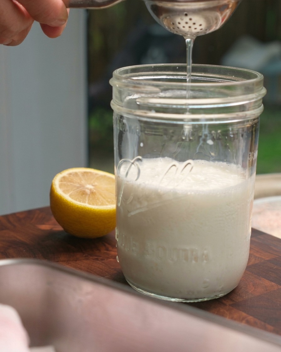 Fresh lemon juice being squeezed from a citrus press into a glass mason jar filled with milk.