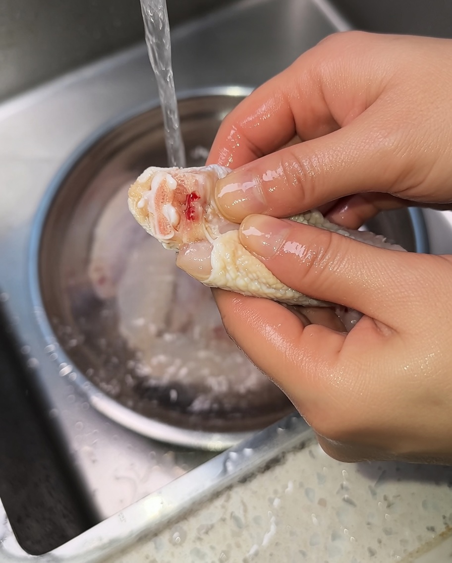 Close-up of hands squeezing a raw chicken wing to expel blood from the joint.