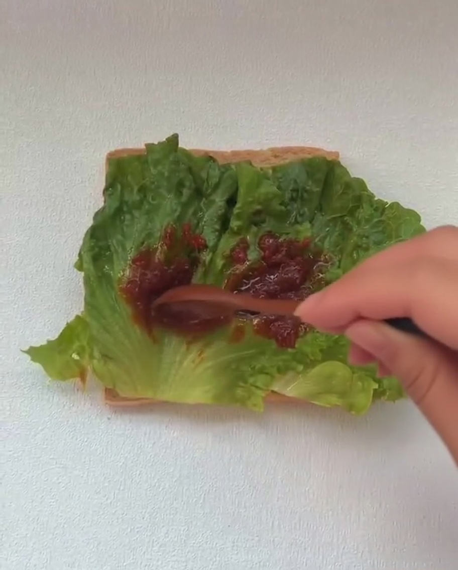 A cooked fried egg being added to a sandwich build, sitting on a layer of green lettuce.