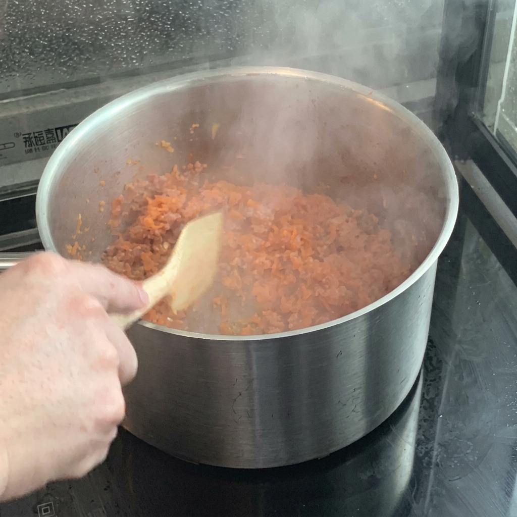 Ketchup being mixed into the sautéed carrots and onions in the pot.