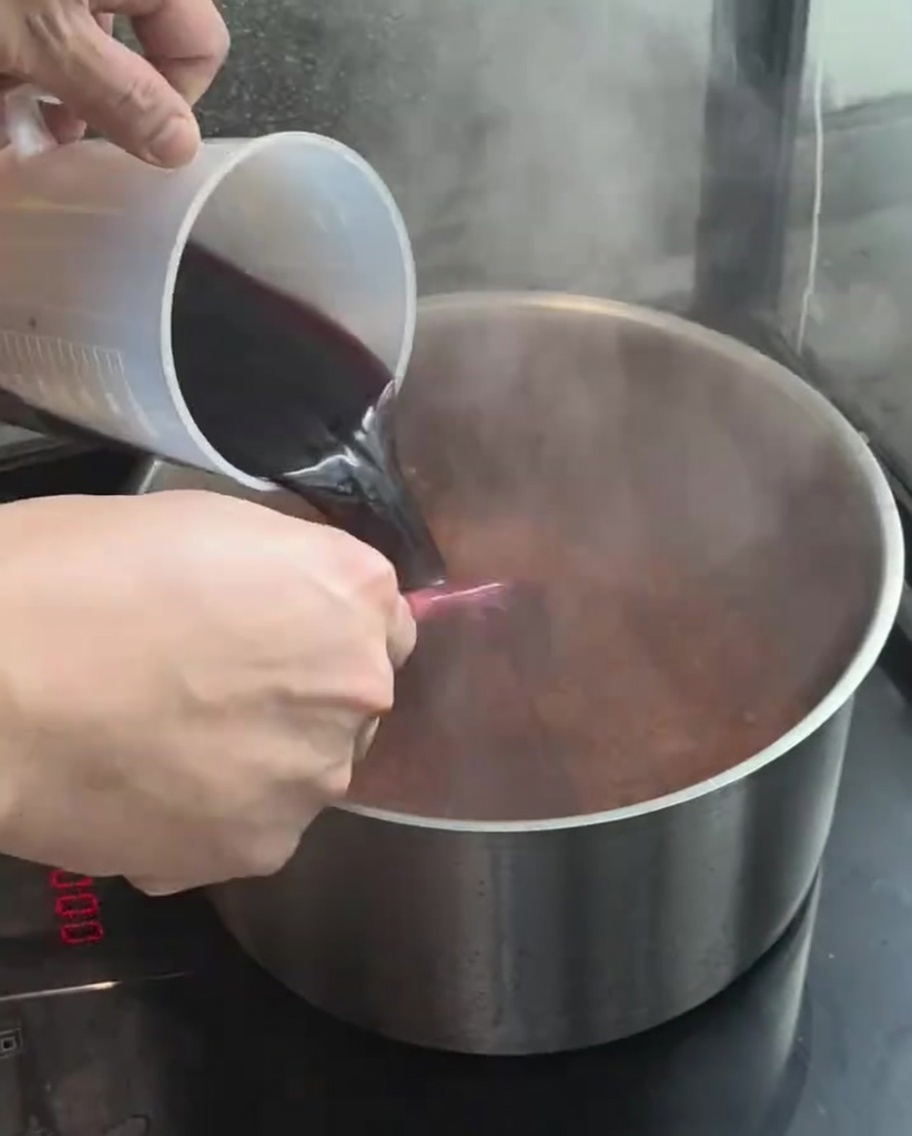 Red wine being poured from a measuring cup into the pot with the carrot and onion mixture.