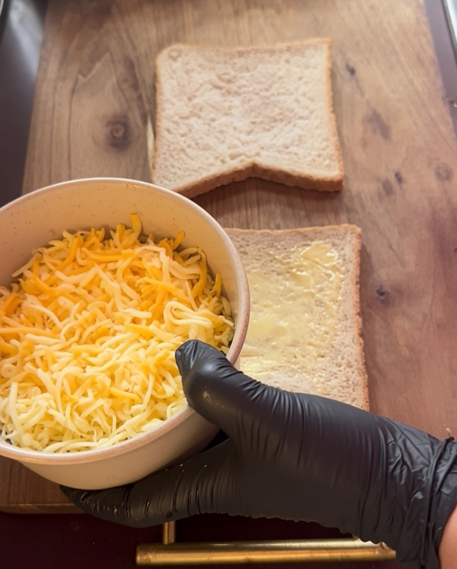 Shredded cheese being layered onto buttered bread slices.