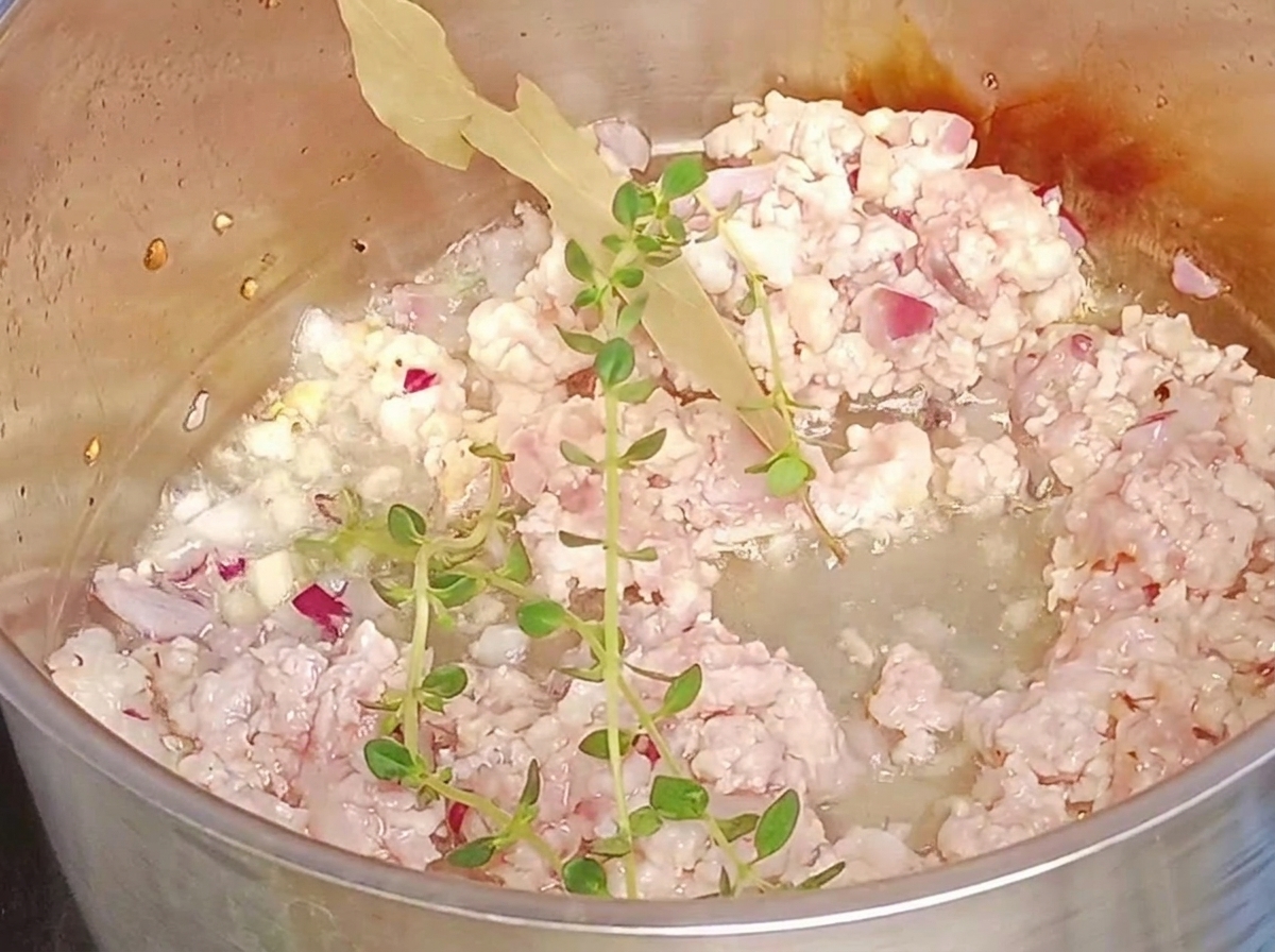 Fresh sprigs of thyme and a bay leaf added to ground meat in a pot.